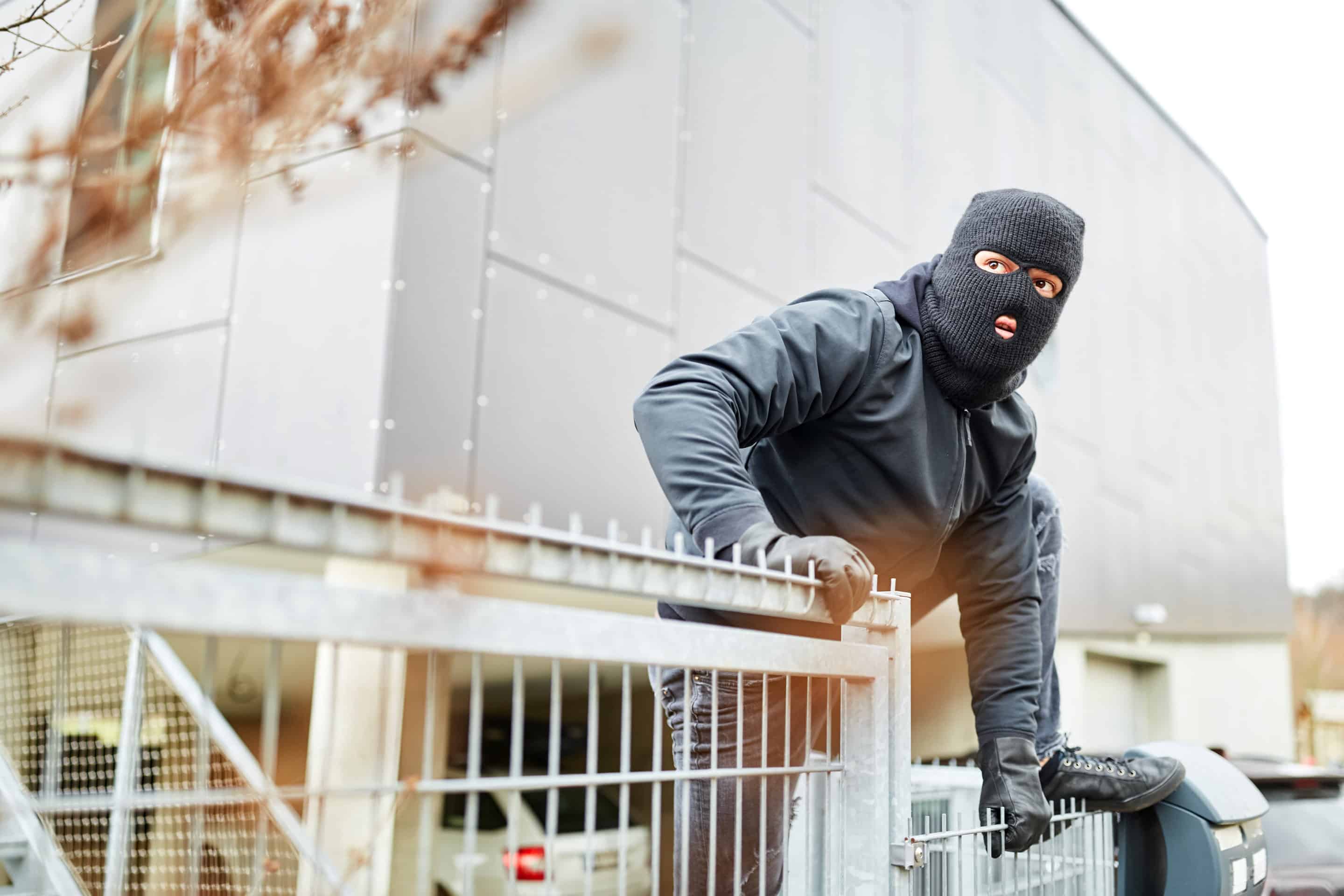 Einbrecher steigt über Zaun von Industrie Firma AdobeStock 279298715 scaled