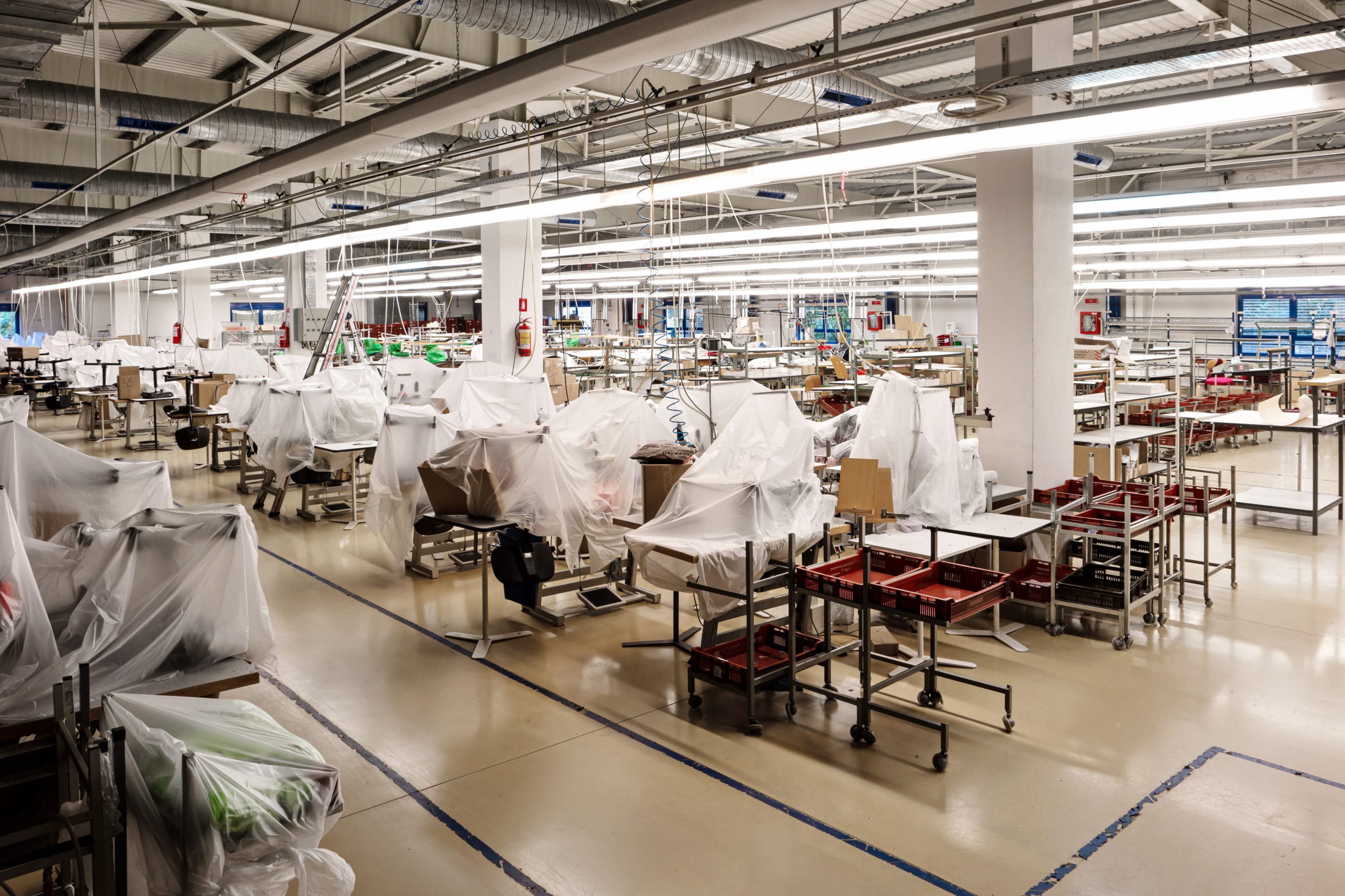 Small out of business garment factory production lines with groups of industrial sewing machines covered up in foil and carton Mobile phone showing 911